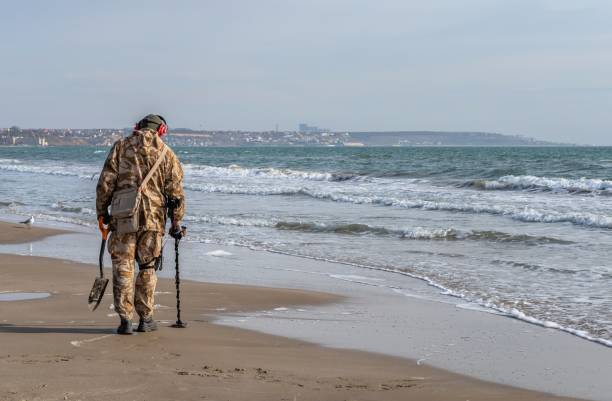Treasure hunt on the beach with a metal detector Odessa, Ukraine 07.02.2022. A man look for valuables using metal detector on the Luzanivka beach in Odessa, Ukraine, on a sunny winter day odessa beach stock pictures, royalty-free photos & images