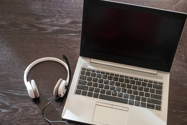 istock Headset on a laptop, blank screen, wooden table background, 1369690677
