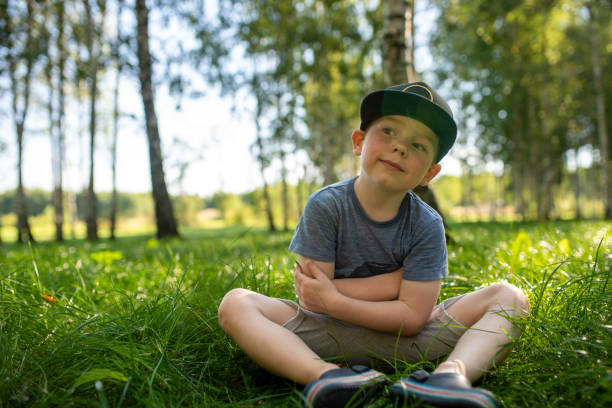 Cute red-haired boy sits on a grass at public park