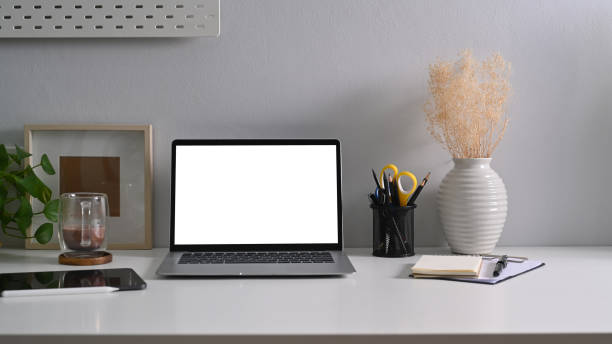 istock Front view laptop computer with blank display, notebook, coffee cup and houseplant on white table. 1369691530