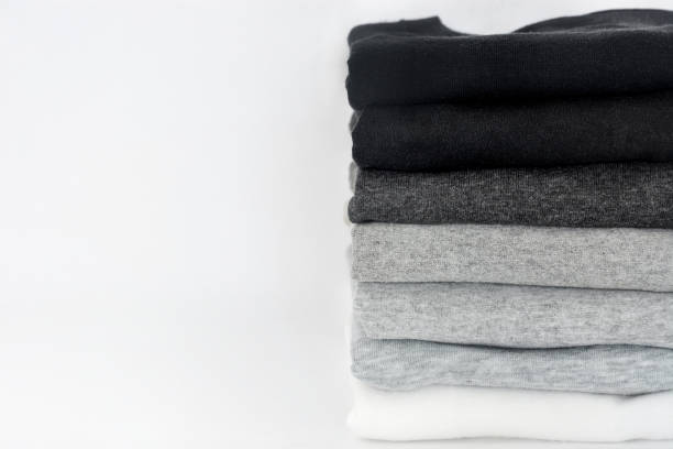 stack of folded black, grey and white color (monochrome) t-shirts on white background, copy space