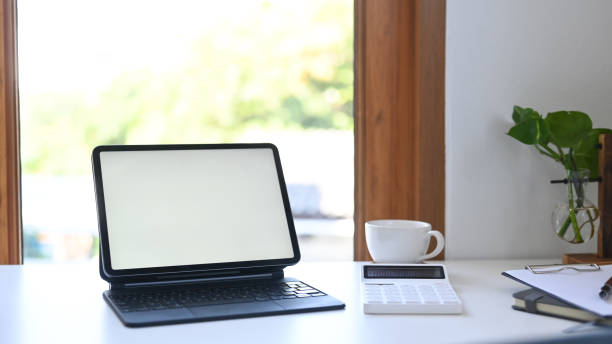 istock Mock up digital tablet with blank screen, calculator, coffee cup and documents on white table. 1369691694