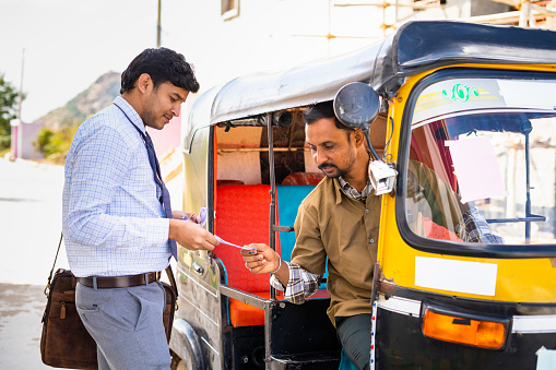 Passenger paying money to auto rickshaw driver after ride - concept of earnings, transportation and commutation.