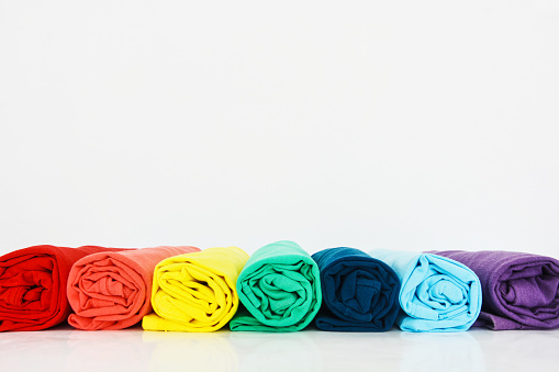stack of colorful t-shirts rolled up on white background, copy space