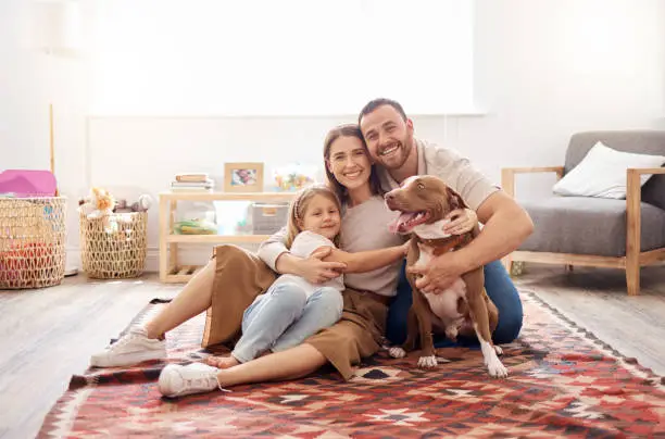 Photo of Full length shot of a young family sitting with their dog on the living room floor at home