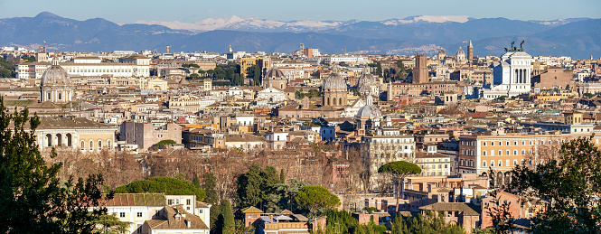 A suggestive and majestic cityscape on the roofs and domes of the historic center of Rome, taken from the top of the Janiculum hill, in the core of the Eternal City. In the background, on the horizon, the snow-capped mountains of the central Apennines and the Abruzzo region. On the right emerges the white shape of the National Monument of the Altare della Patria, while on the top left the building of the Presidential Palace of the Quirinale. In 1980 the historic center of Rome was declared a World Heritage Site by Unesco. Image in high definition in wide format.