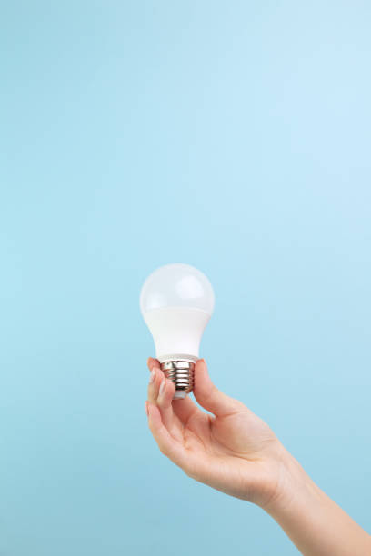 Female hand holds an LED lamp on a blue background. Energy saving concept, alternative energy sources, idea Female hand holds an LED lamp on a blue background. Energy saving concept, alternative energy sources, idea energy efficient lightbulb stock pictures, royalty-free photos & images