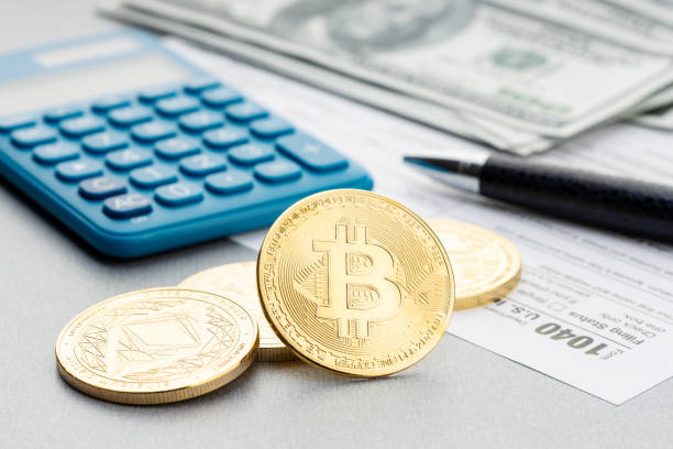 Cryptocurrency coins, calculator and 1044 tax form on table. Bitcoin Tax time concept stock photo