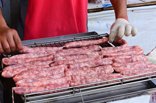 chef putting fresh raw sausage grilling outdoors on a gas barbecue grill. street food, Taiwan
