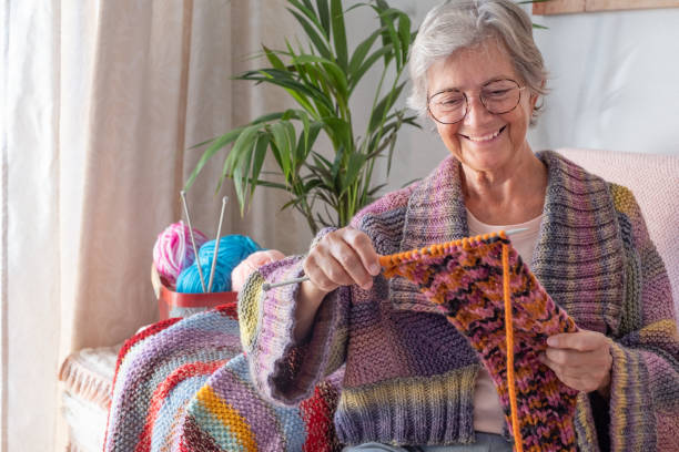 istock Senior smiling woman sitting on sofa at home while knitting and looking at her work in progress. Hobby, retirement, relax concept for elderly female wearing glasses 1369701067