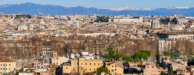 A suggestive and majestic cityscape on the roofs and domes of the historic center of Rome, taken from the top of the Janiculum hill, in the core of the Eternal City. In the background, on the horizon, the snow-capped mountains of the central Apennines and the Abruzzo region. In the center emerges the dome of the Roman Pantheon, while at the top right the white building of the Presidential Palace of the Quirinale. In 1980 the historic center of Rome was declared a World Heritage Site by Unesco. Image in high definition in wide format.