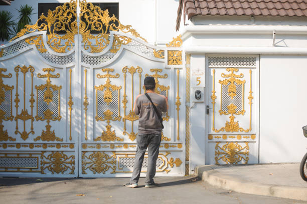 Express delivery man of Kerry is waiting at gate of a residential home in Bangkok Chatuchak. At right side if man is a video camera at wall and door. Gate is in thai arts ornated