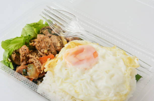 Jasmine rice with spicy pork fried with thai pepper and fried egg in a transparent plastic box package, ready to eat