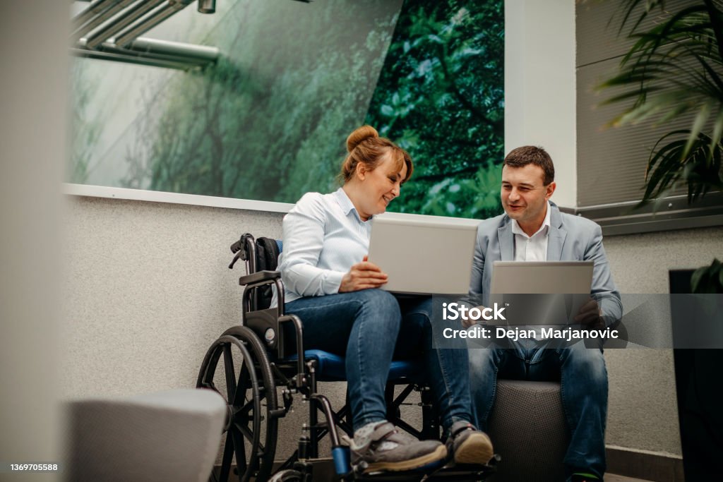 Working in wheelchair Taking a break with colleague in wheelchair using laptop Accessibility Sign Stock Photo