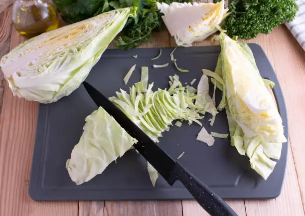 Cutting and chopping of fresh and raw white cabbage. Served with kitchen knife on a cutting board.