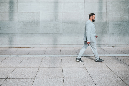 elegant bearded senior business man walking in city in front of wall