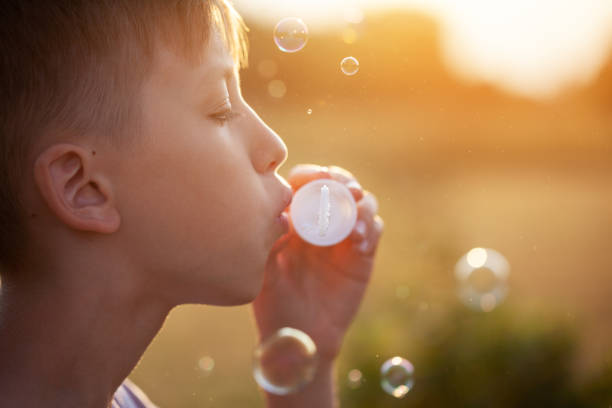 istock Child blowing soap bubbles at sunset on a summer day. Boy playing on nature. 1369713646