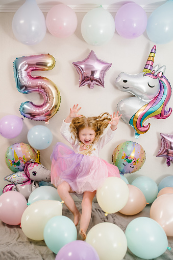 Happy and surprised girl celebrates her birthday. Party decoration with balloons in the style unicorn, rainbow, my little pony. Birthday party for 5 years. Idea for decorating party.