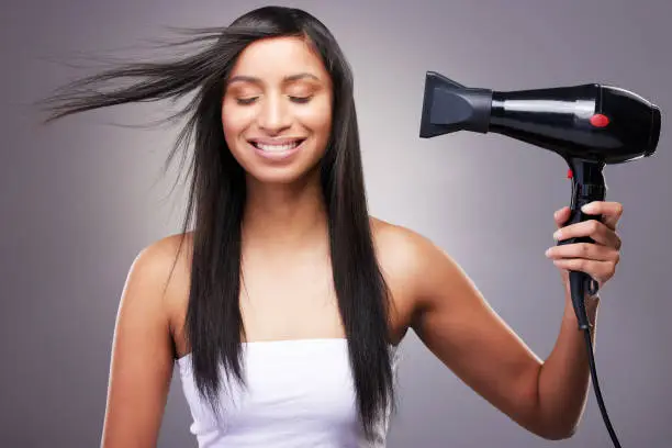 Photo of Shot of an attractive young woman standing alone in the studio and using a hairdryer