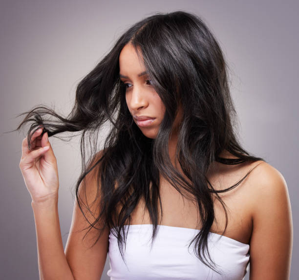 Shot of an attractive young woman standing alone in the studio and feeling frustrated while looking at her hair Oh look, split ends frizzy stock pictures, royalty-free photos & images