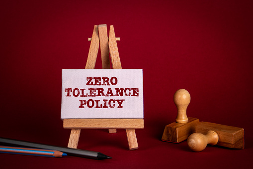 Política de Tolerancia Cero. Caballete en miniatura y sellos de madera sobre un fondo rojo brillante photo
