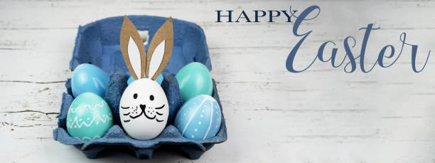 istock Happy Easter background banner panorama greeting card -Close-up from colorful painted eggs / easter bunnies in blue egg carton on rustic white vintage shabby wooden table 1369718373