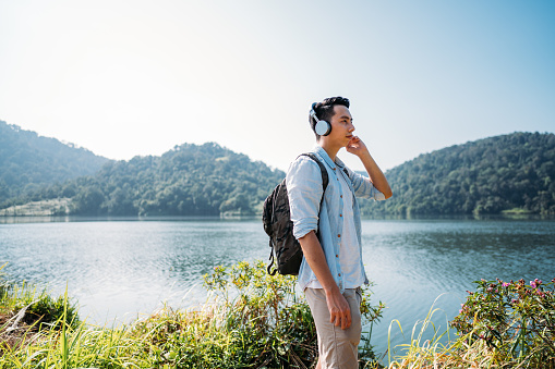 Relaxation in mountains. Young Asian man with headphones looking at lake scenery and listening music. Rainforest, Malaysia