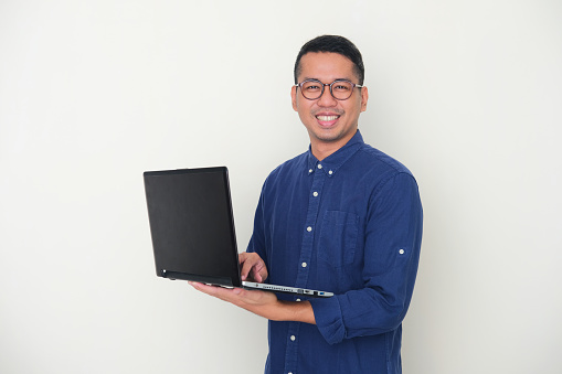 istock Adult Asian man looking to the camera while holding a laptop and showing happy expression 1369719651