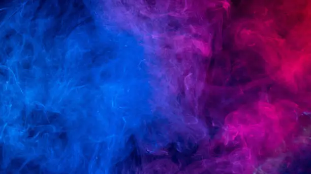 Photo of Conceptual image of colorful red and blue color smoke on dark black background.