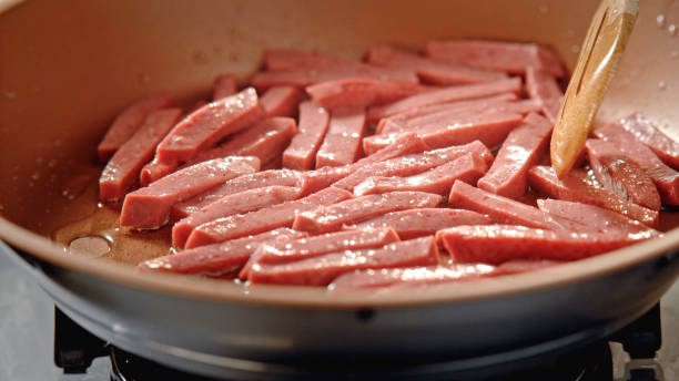 in scheiben geschnittene salami werden in einer pfanne gebraten. - wurst stock-fotos und bilder