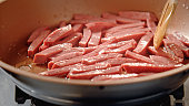 Sliced salamis are fried in a pan.