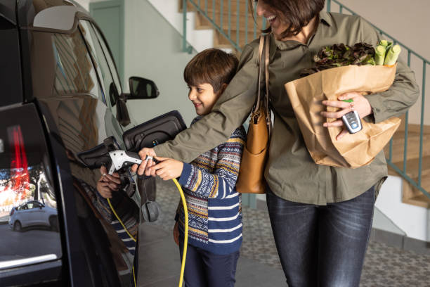 мать и сын заряжают электромобиль дома. - electric vehicle charging station стоковые фото и изображения