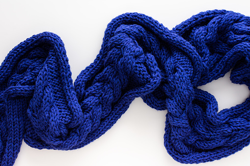 Blue knitted woolen scarf on a white background, homemade needlework concept, copy spase