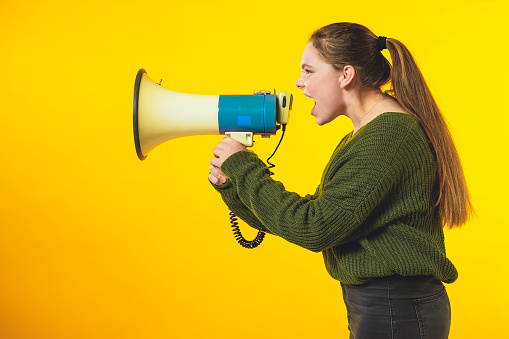 Young girl with megaphone shouting! Isolated on yellow background with copy space