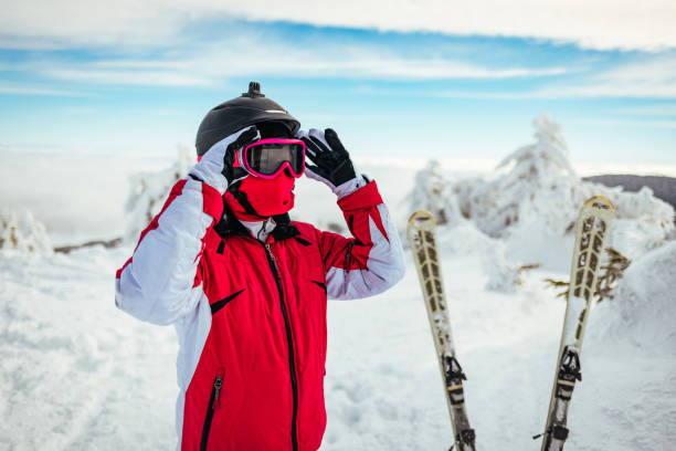 A young attractive woman in a ski suit is wearing a helmet. In the background of snow-capped mountains