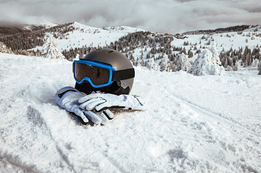 Helmet, gloves and ski goggles on snow with a blue sky and mountains