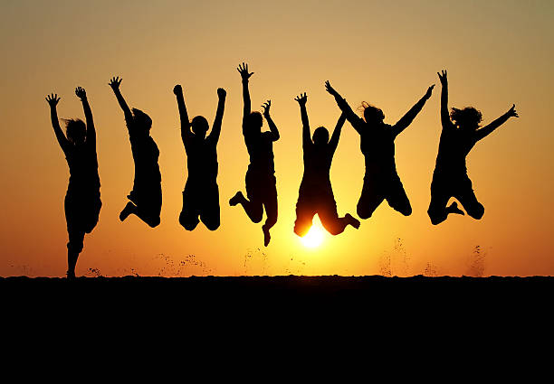 silhouette of friends jumping in sunset stock photo