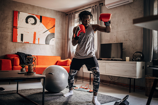 One man, handsome black male boxer exercising with boxing gloves in living room at home.