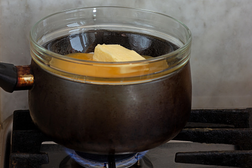 Bain-marie with sugar, butter and honey in glass bowl on saucepan as ingredients of cake medovik on stovetop