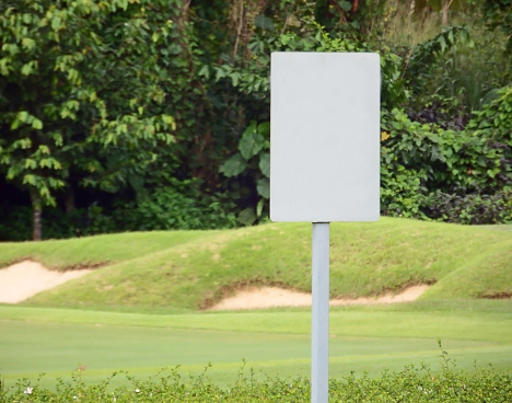 Blank white rectangular sign on a post on a golf course with fairway grass and bunkers in the background
