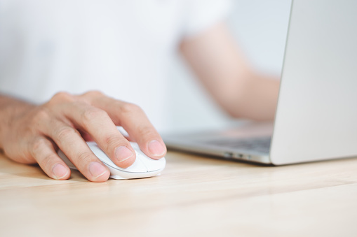 Man using computer mouse with laptop on wooden table