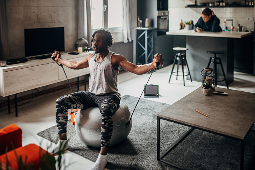 One man, handsome black man exercising in living room at home. Woman is in kitchen behind him.