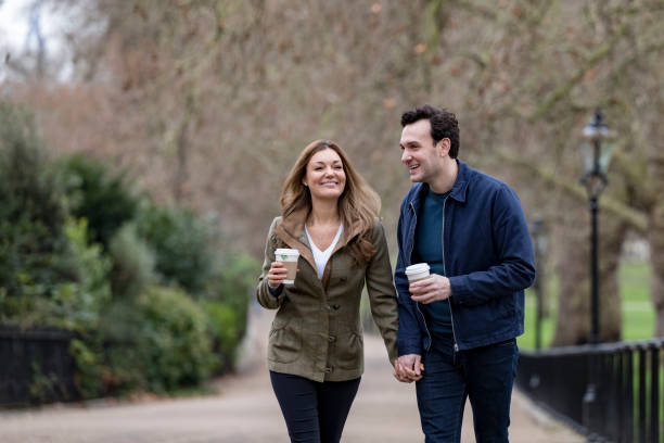 Smiling couple holding hands and walking in park with coffee