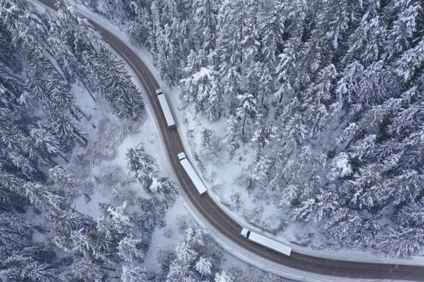 Convoy of Trucks Moving During Snowfall on a Winding Curving Winter Mountain Road stock photo