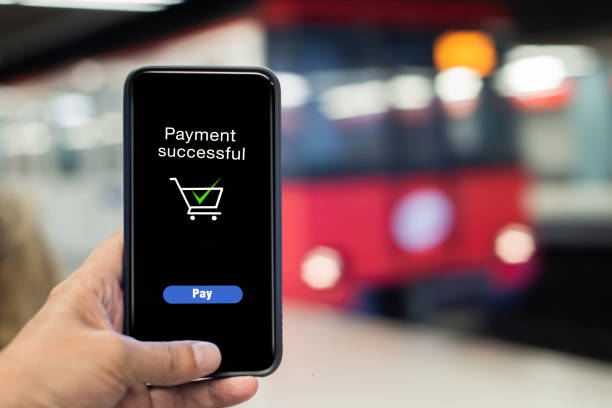 The hand with the smartphone makes the payment while waiting on the subway platform stock photo