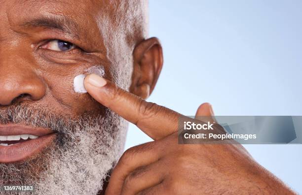 Studio Portrait Of A Mature Man Applying Moisturiser To His Face Against A Blue Background Stock Photo - Download Image Now