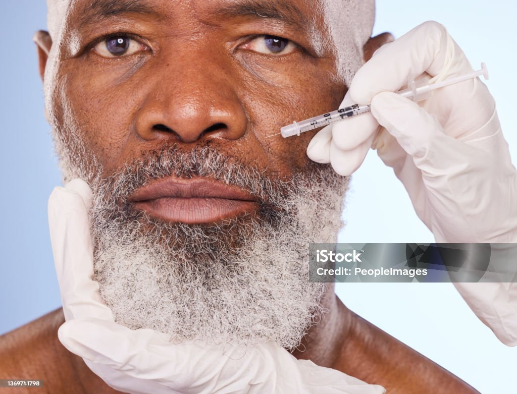 Portrait en studio d’un homme mûr se faisant injecter le visage par des mains gantées sur un fond bleu - Photo de Injection de toxine botulique libre de droits