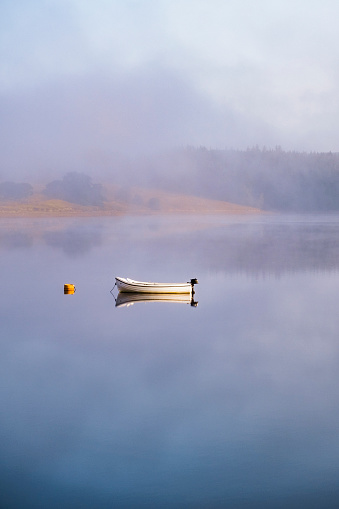 A small motor boat resting on a calm lake in the fog.