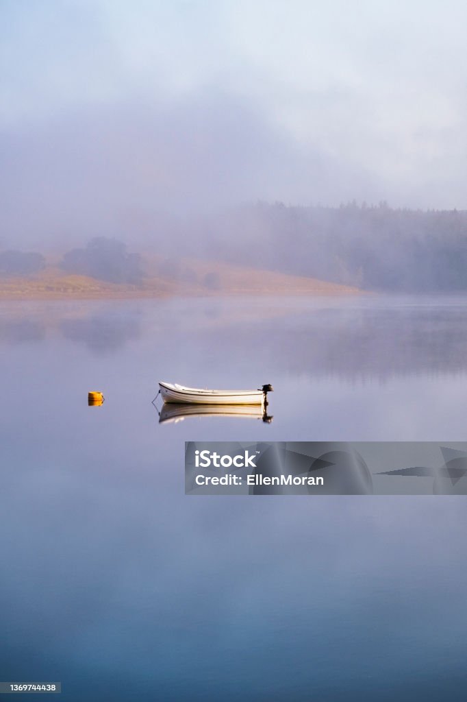 Small boat resting in the calm water A small motor boat resting on a calm lake in the fog. Tranquility Stock Photo