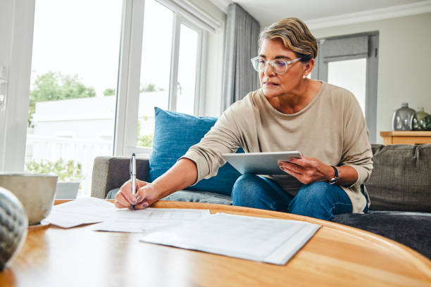 Shot of a mature woman using a digital tablet while going through paperwork at home Put it on paper and it'll become a reality filling out stock pictures, royalty-free photos & images